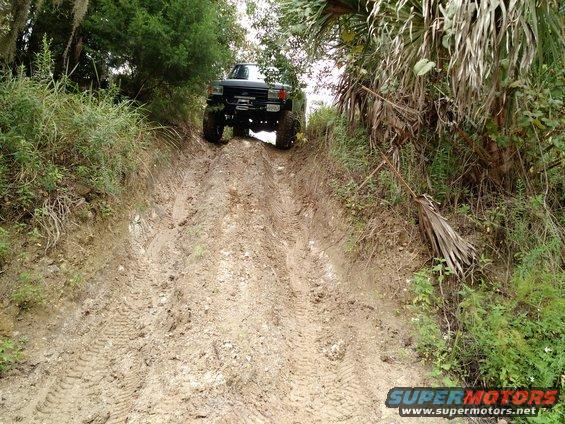Truck going up a muddy trail, looks like a Ford Bronco from the late 80s