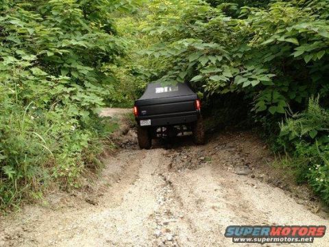1989 Ford Bronco - A black SUV navigates a rough dirt road through dense foliage.
