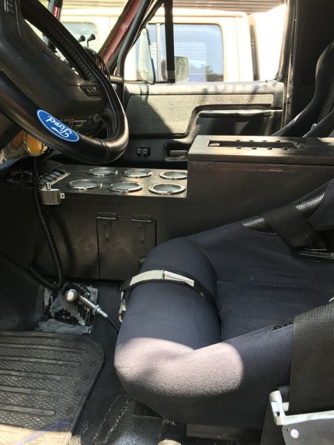 1989 Ford Bronco - The interior of a vehicle features a Ford steering wheel and a custom center console with multiple cup holders.