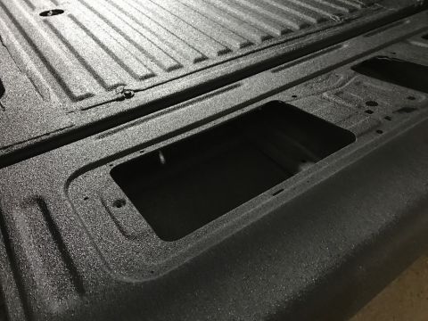 1989 Ford Bronco - Close-up of a textured black truck bed liner, showing ribbed patterns and recessed areas.
