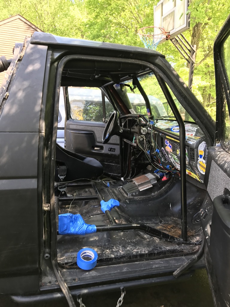 Black 1989 Ford Bronco interior with removed seats, exposed wiring, and blue tape on the floor