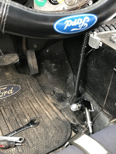 1989 Ford Bronco - The interior of a vehicle features a Ford-branded steering wheel and floor mat, with visible pedals and aftermarket wiring.