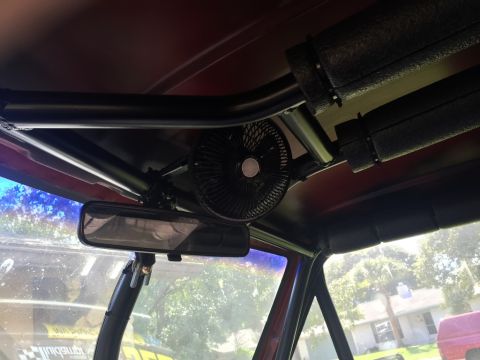1989 Ford Bronco - A close-up of a vehicle's interior reveals a mounted fan and rearview mirror, with roll cage elements overhead.