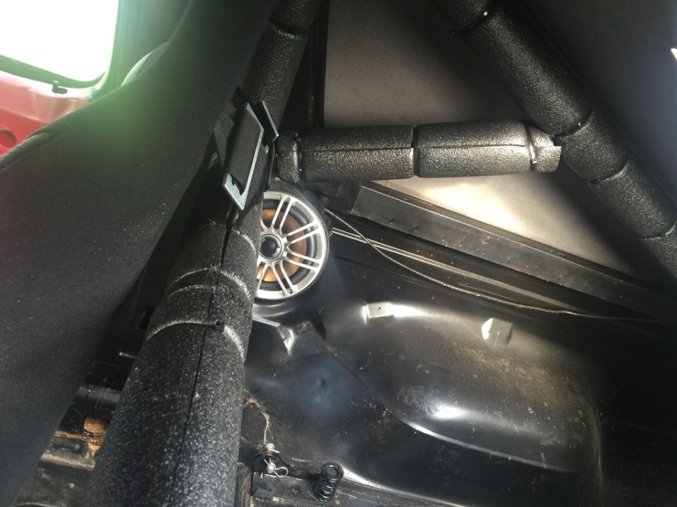 Interior view of a vehicle with black roll bar padding and a silver speaker. A red seat is partially visible