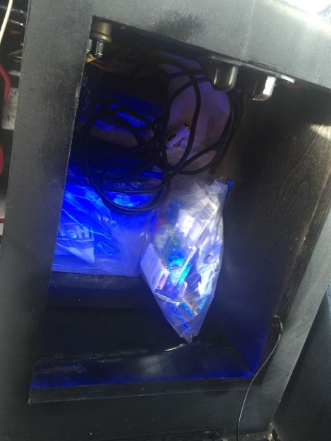 1989 Ford Bronco - A dark storage area is illuminated by blue lights, revealing coiled wires and a plastic bag filled with small objects.