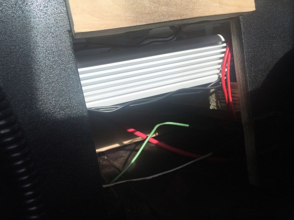 Car amplifier with fins and red and green wires visible inside a dark interior compartment