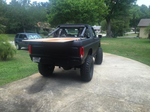 1989 Ford Bronco - This modified black Ford Bronco, likely from the late 1980s, is parked in a driveway with another SUV in the background.