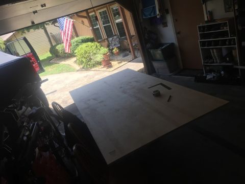 1989 Ford Bronco - A garage scene shows a large sheet of plywood on the floor, with tools like a tape measure and speed square nearby.