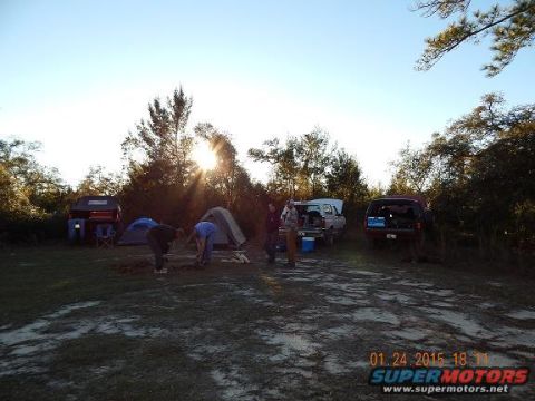 1989 Ford Bronco - A campsite scene unfolds with two SUVs parked near tents, bathed in the warm glow of the setting sun.