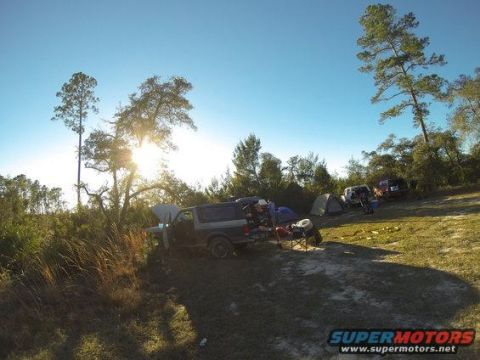 1989 Ford Bronco - A campsite scene with a Ford Bronco, tents, and other vehicles under a clear blue sky.