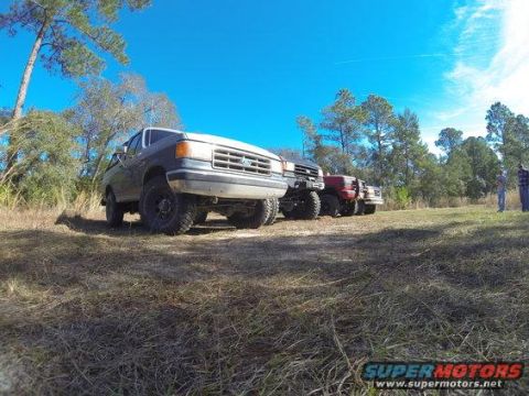 1989 Ford Bronco - Several trucks, including a 1989 Ford Bronco, are lined up outdoors on a sunny day.