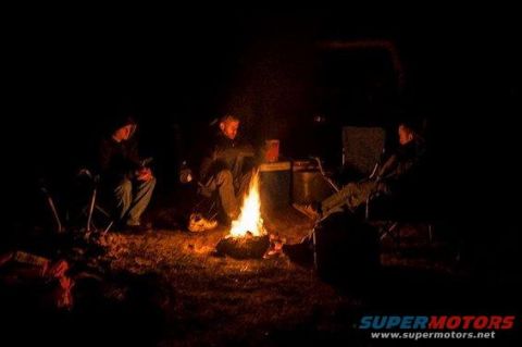 1989 Ford Bronco - A group of people enjoy a campfire at night, with a dark vehicle visible in the background.