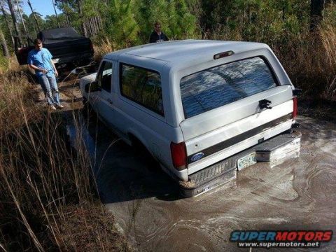 1989 Ford Bronco - A white 1989 Ford Bronco is stuck in the mud with another vehicle visible behind it.
