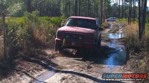 1989 Ford Bronco - Red 1989 Ford Bronco navigating a wet, muddy path in a wooded area.