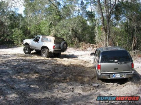 1989 Ford Bronco - Two SUVs navigate a sandy trail in a wooded area, one a lifted white 1989 Ford Bronco and the other a silver SUV.