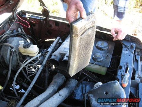 1989 Ford Bronco - A person is removing a very dirty air filter from the engine compartment of a vehicle.