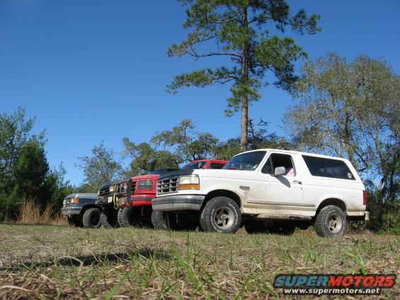 White 1992 Ford Bronco parked in a field with three other SUVs behind it
