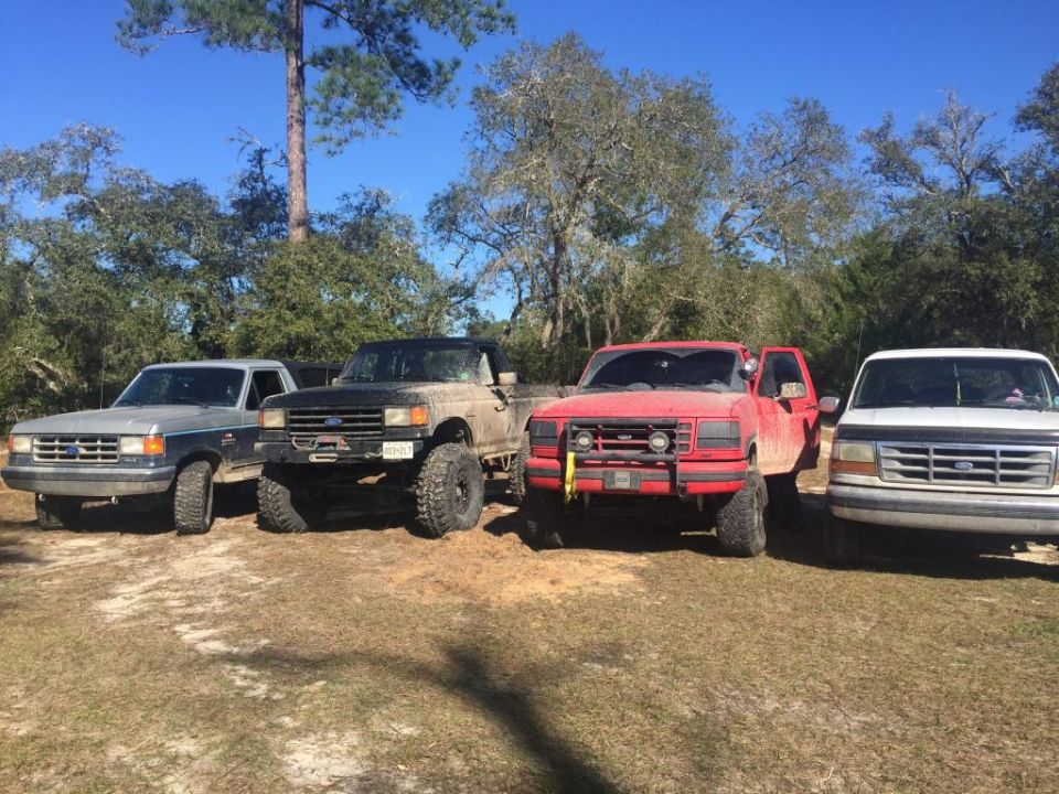 Four pickup trucks, including a red Ford F-150 from the late 1980s, parked outdoors