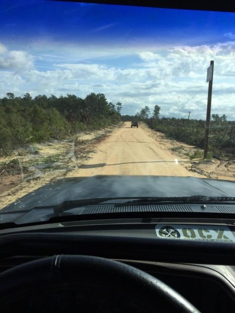 1989 Ford Bronco - View from inside a vehicle driving on a dirt road with another SUV ahead, surrounded by trees and brush.