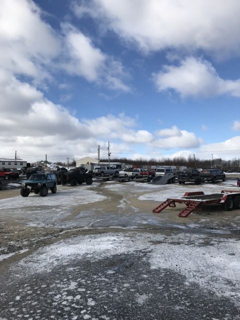 1989 Ford Bronco - A variety of trucks and trailers are parked in an outdoor lot under a cloudy sky.