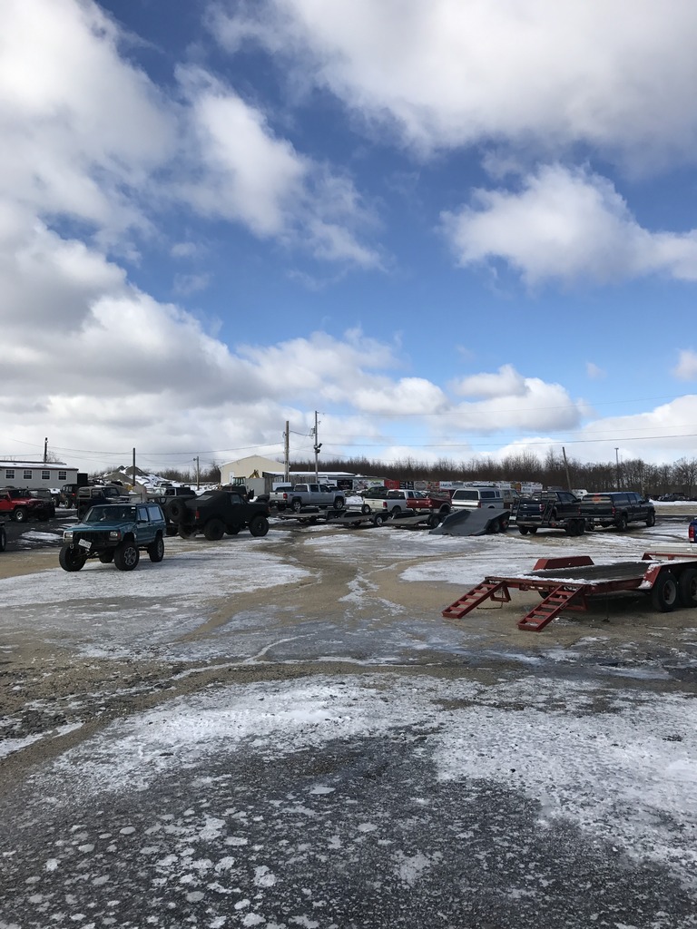 Several off-road vehicles and trailers parked in a lot with snow on the ground