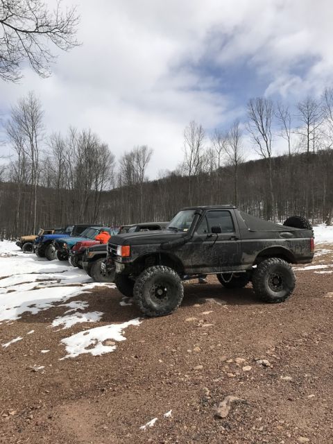 1989 Ford Bronco - Several off-road vehicles are lined up on a snowy, wooded trail.