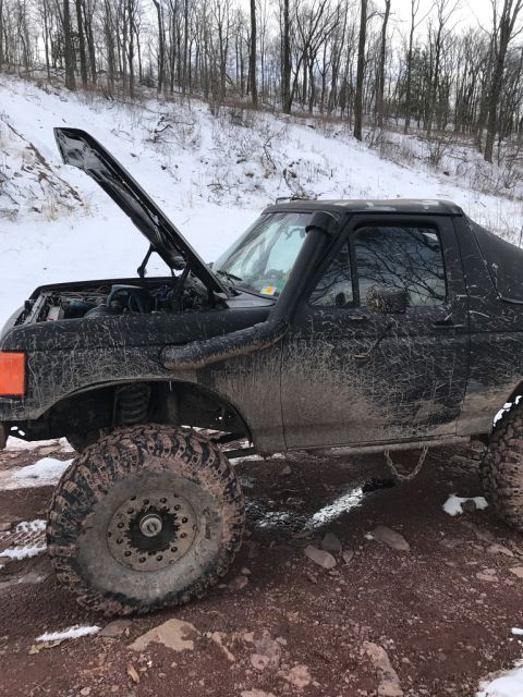 1989 Ford Bronco - A black 1989 Ford Bronco is shown with its hood open and a snorkel attachment, ready for off-road adventure in a snowy, muddy environment.