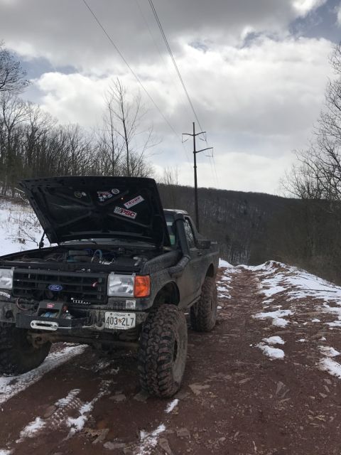 1989 Ford Bronco - Off-road Bronco on a snowy trail, hood up revealing the engine bay.