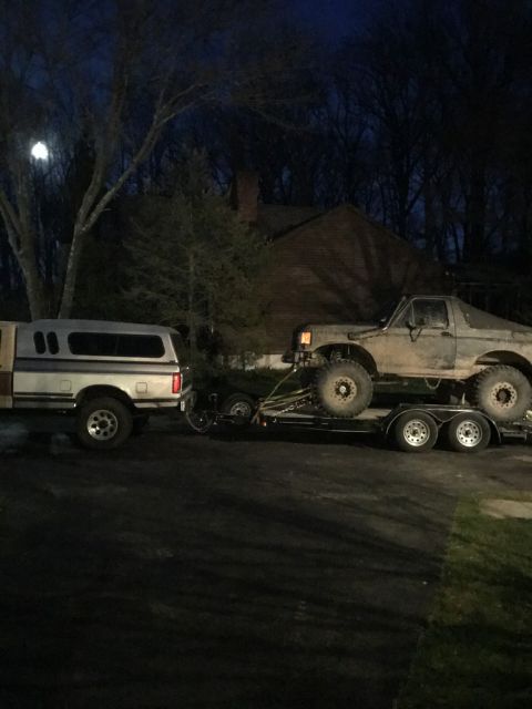 1989 Ford Bronco - A lifted Ford Bronco is transported on a trailer behind a pickup truck at night.