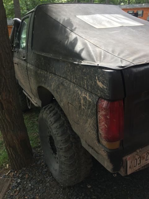 1989 Ford Bronco - This SUV, likely from the 1980s, is covered in mud and has a soft top and large tires.
