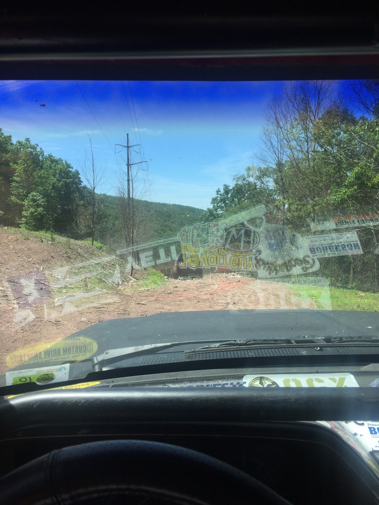 View from inside a vehicle looking out at a dirt road with trees and a power line tower