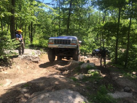 1989 Ford Bronco - A blue Ford Bronco tackles an off-road course with another vehicle visible in the background.