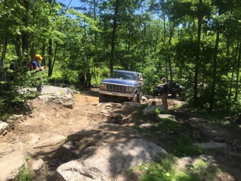 1989 Ford Bronco - A blue SUV navigates a challenging rocky trail with another vehicle in the background.