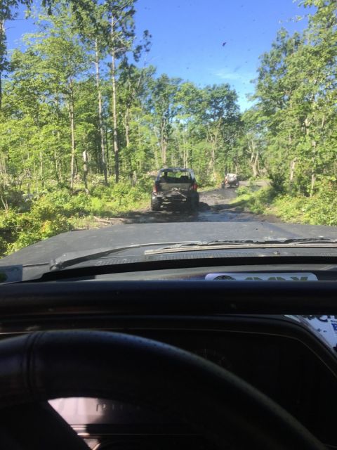1989 Ford Bronco - Multiple vehicles navigate a muddy off-road path surrounded by trees.