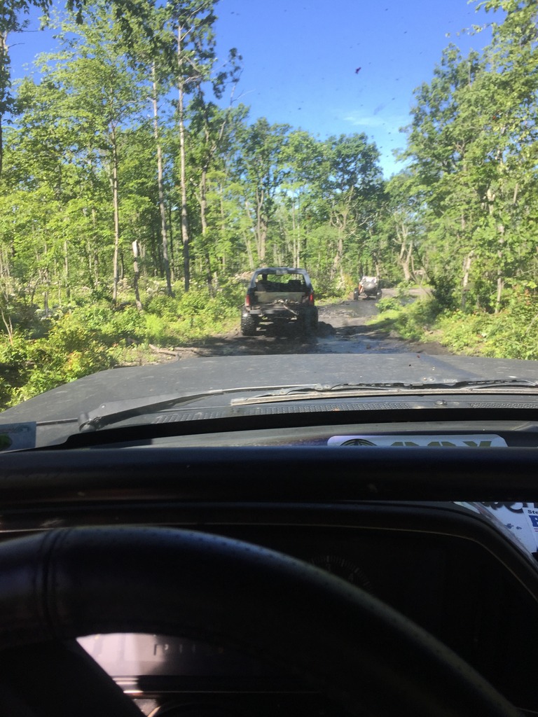 Black Ford Bronco driving on a muddy trail, viewed from inside another vehicle