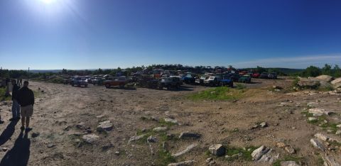 1989 Ford Bronco - A large collection of SUVs and trucks are parked on a dusty, rocky terrain under a clear blue sky.