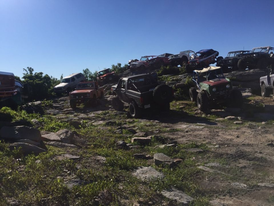 Several off-road vehicles parked and driving on a rocky hill under a clear blue sky