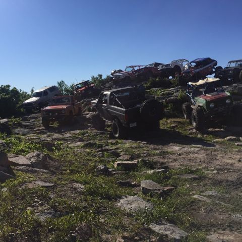 1989 Ford Bronco - A group of off-road vehicles navigate a challenging rocky incline on a sunny day.