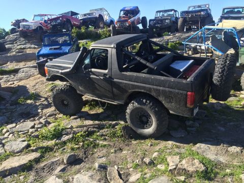 1989 Ford Bronco - Multiple off-road vehicles are parked on a rocky hill under a clear blue sky.