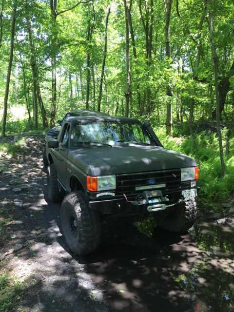 1989 Ford Bronco - This modified 1989 Ford Bronco navigates a wooded trail with large off-road tires and a winch.