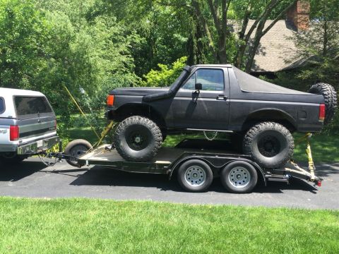 1989 Ford Bronco - A black Ford Bronco is transported on a trailer behind a silver pickup truck.
