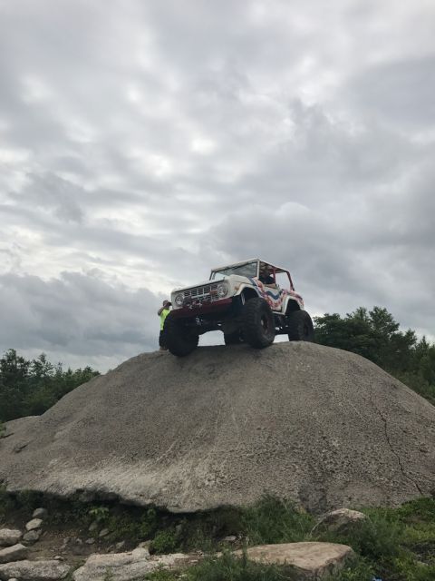 1989 Ford Bronco - White Ford Bronco with red and blue graphics climbs a large rock formation under a cloudy sky.