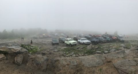 1989 Ford Bronco - A large group of off-road vehicles are gathered on a rocky, uneven surface, obscured by thick fog.