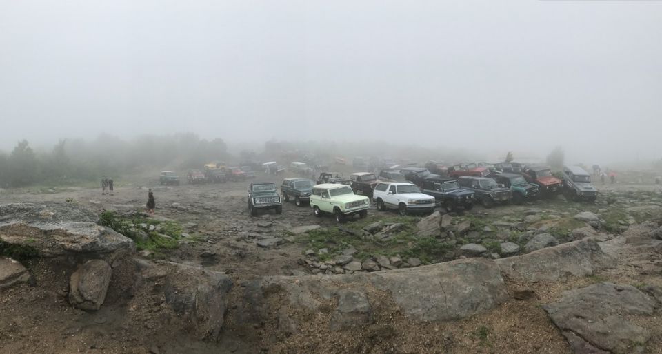 many SUVs and trucks parked on rocky terrain in heavy fog