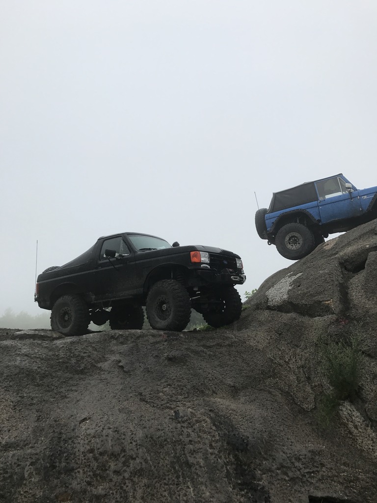 Black Bronco and blue Bronco climbing rocks. Black one is in foreground