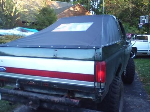 1989 Ford Bronco - Rear view of a dark green Ford Bronco with a soft top and distinctive red and white stripe on the tailgate.