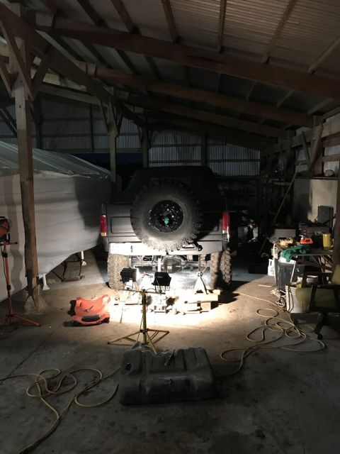 1989 Ford Bronco - A gray Ford Bronco is undergoing repairs in a garage, with its rear end lifted and spare tire visible.