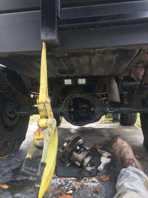 1989 Ford Bronco - A differential is shown removed from a vehicle's rear axle, with a yellow ratchet strap attached to the frame.