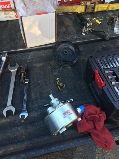 1989 Ford Bronco - A new power steering pump, pulley, and assorted tools are laid out on a truck bed, likely for installation or repair.