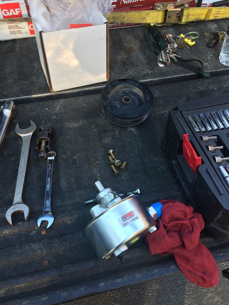 Power steering pump with part number SN1-11699, pulley, wrenches, and socket set on a truck bed